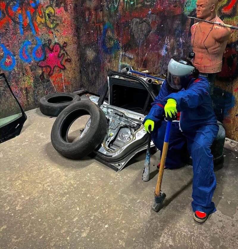 man posing with a hammer and a baseball bat in rage room