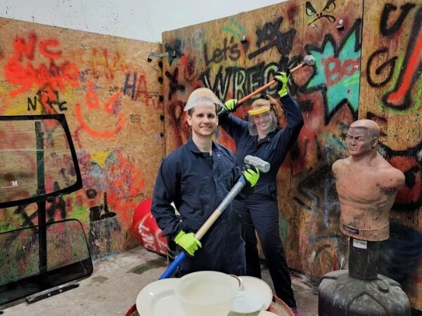 couple holding hammers and posing for a picture in a rage room